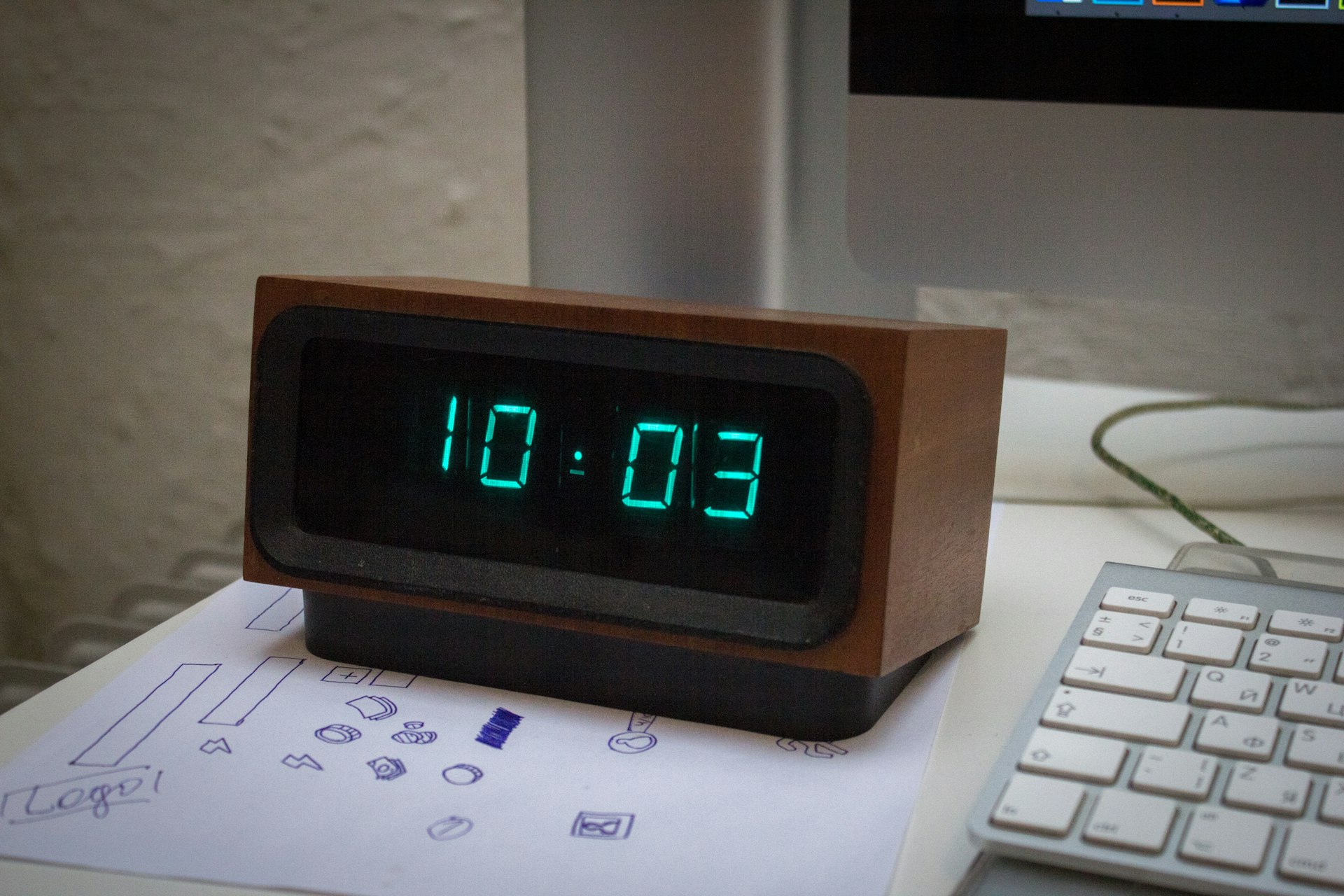 A digital clock sitting on top of a desk next to a keyboard